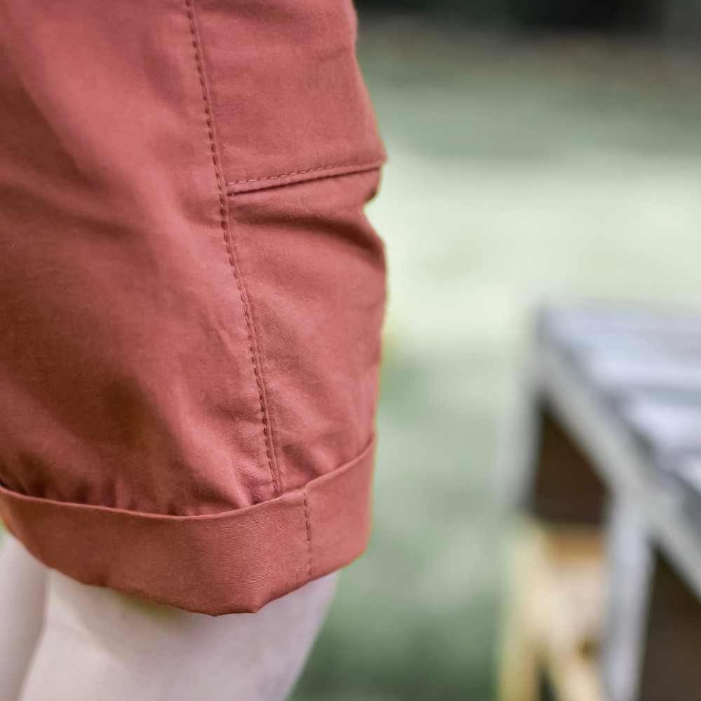 Gros plan sur le revers et la poche latérale plaquée d'un bermuda enfant en coton terracotta, porté par un garçon