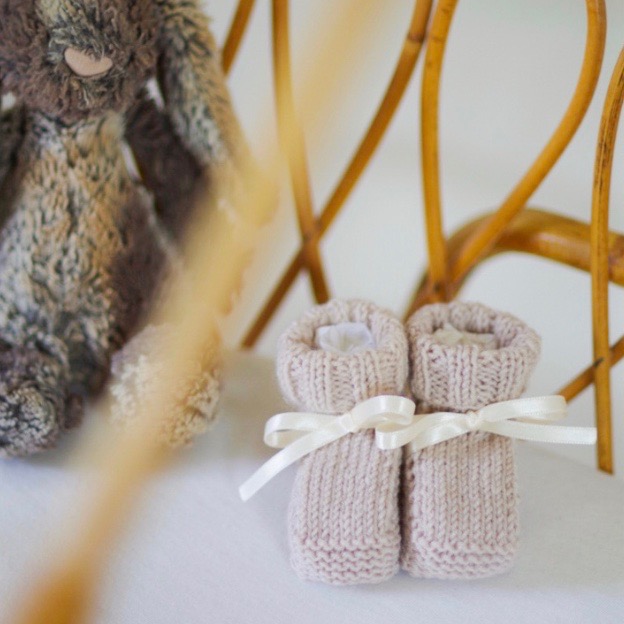 Zoom sur des chaussons tricotés en coton bio écru et leur ruban en satin