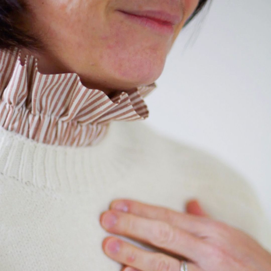 Col amovible à l'imprimé avec des rayures fines écrues et caramel au beurre salé glissé sous un pull écru et porté par une femme