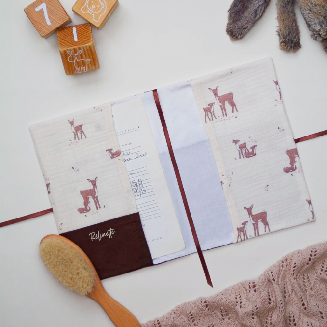 L'intérieur d'un protège-carnet de santé bébé fait main, en tissu imprimé "Petits faons", posé délicatement dans une ambiance douce et naturelle.