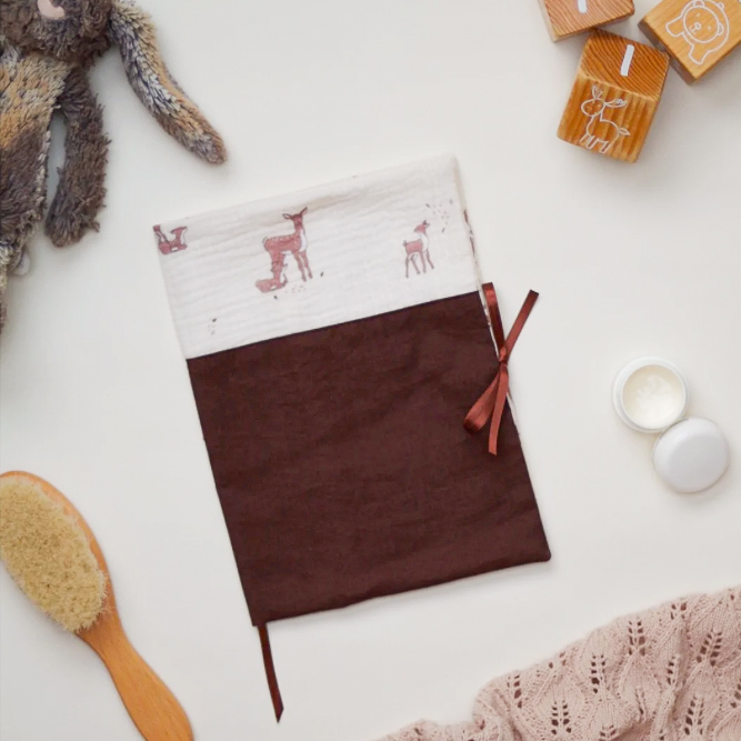 Protège-carnet de santé bébé fait main, en tissu assorti aux autres créations du coffret de naissance Premiers jours, posé délicatement dans une ambiance douce et naturelle.