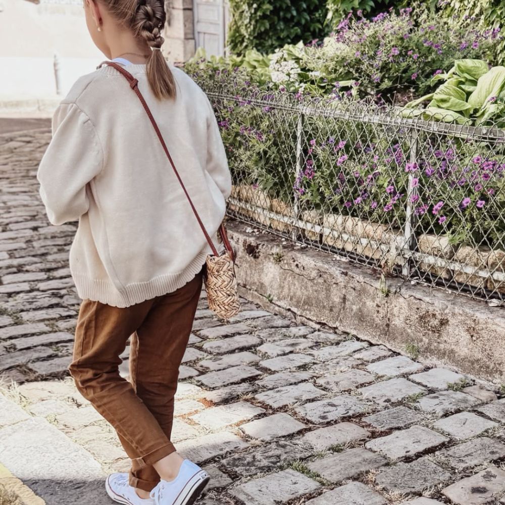 Fillette de dos portant un gilet écru et un pantalon en lin lavé tabac pour une virée shopping entre filles.
