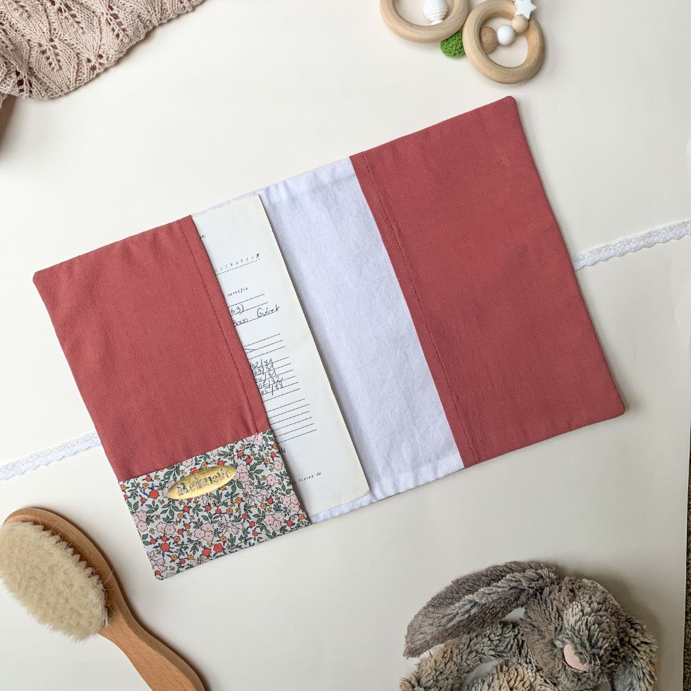 Intérieur d'un protège carnet de santé ouvert en tissu vieux rose uni, avec rabatss latérales pour maintenir le carnet en place. Sur l'un des rabats, il y a une pochette fleurie pour y glisser les ordonnances ou la carte vitale.