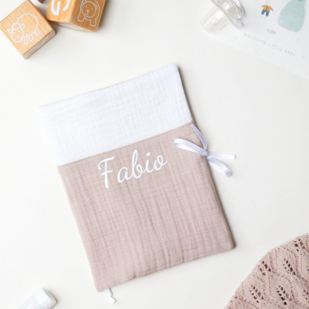 Protège carnet de santé bébé en double gaze bicolore blanc et taupe, personnalisé avec le prénom Fabio brodé en blanc, fermé par un ruban satin blanc